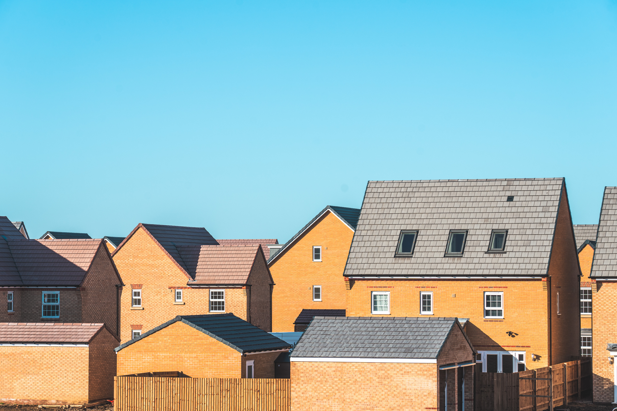 Row of new, brick-built houses with tile roofs against a clear blue sky.